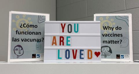 A nurse's sign reads "You are loved" with vaccine activity signs on either side.